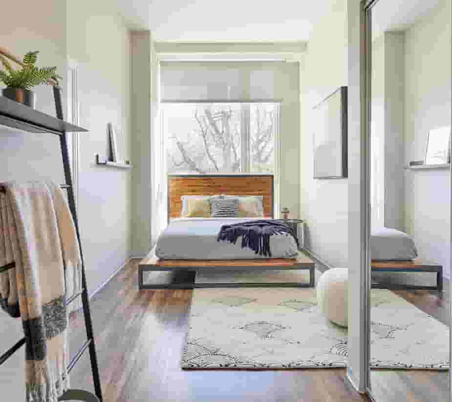 Bedroom with wood-style flooring, mirroed closet doors, and roller shade in window